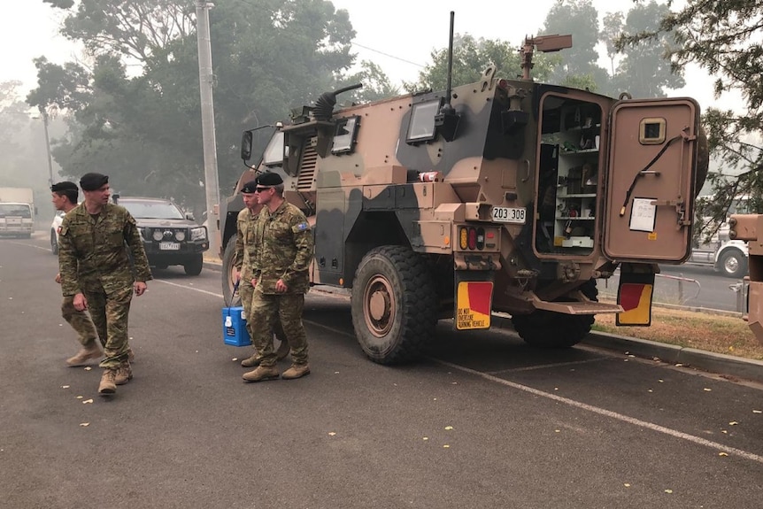 Australian Army troopers wear army fatigues and walking on a road with an army truck behind them.