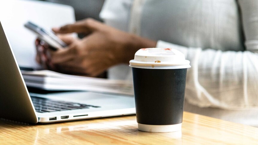 Worker with a takeaway coffee cup next to their computer