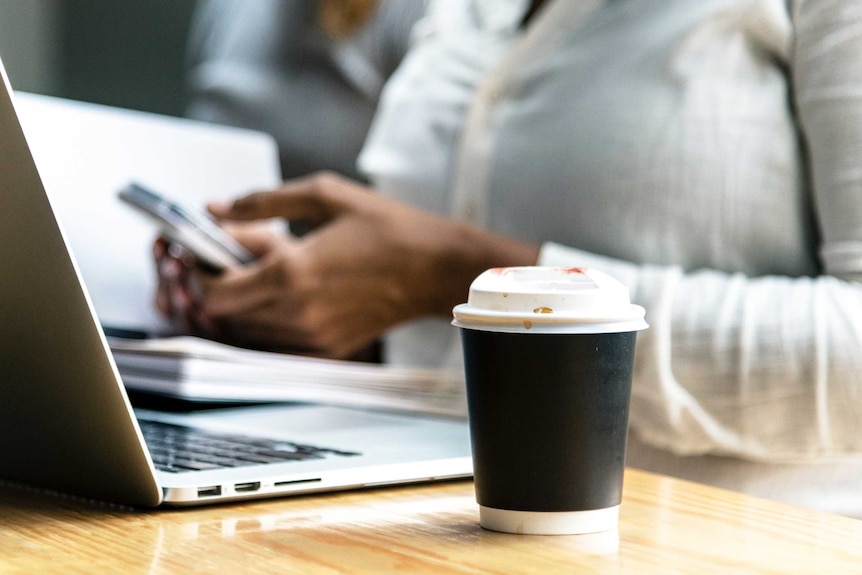 Worker with a takeaway coffee cup next to their computer