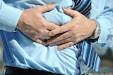 A man in a tie hold his hands over his upper abdomen.