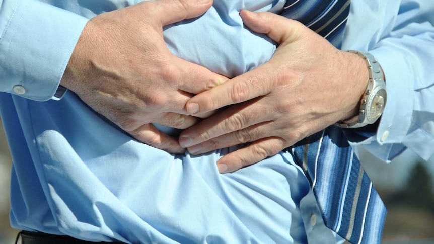 A man in a tie hold his hands over his upper abdomen.