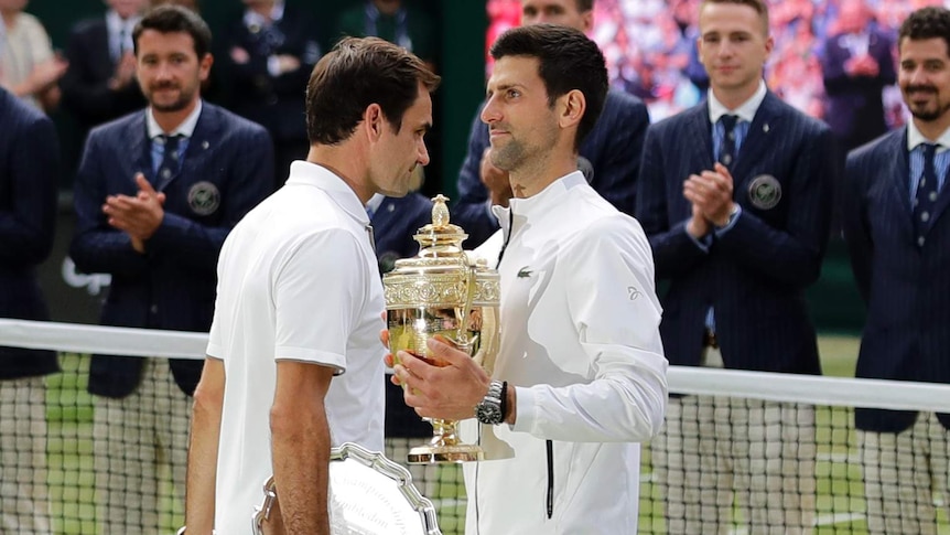 Novak Djokovic holds the Wimbledon trophy as Roger Federer walks past with the runner-up plate