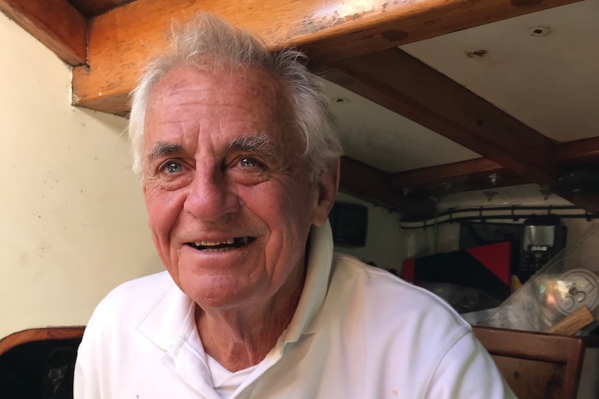 Jon Sanders pictured in white shirt sitting in yacht cabin, smiles at the camera.