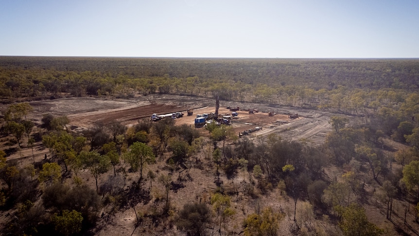 An aerial view of several lines of trucks parked on a large, cleared patch of dirt, surrounded by scrub.