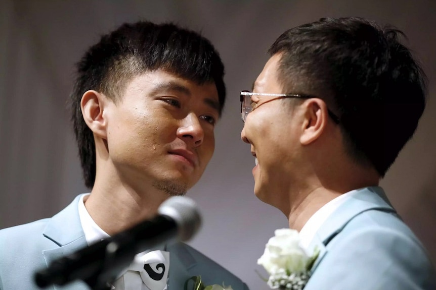 Two men dressed in suits cry happy tears during their wedding ceremony.