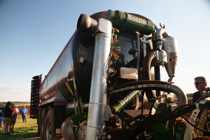 A slurry tanker is sitting in a paddock surrounded by farmers