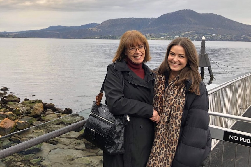 A mother and daughter stand together at the edge of a lake