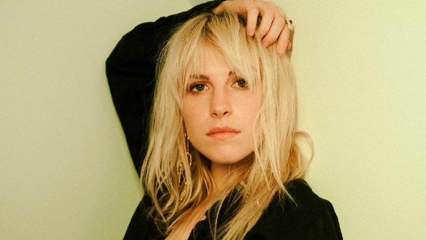 Hayley Williams, with blonde hair, wearing a black shirt and gold jewellry