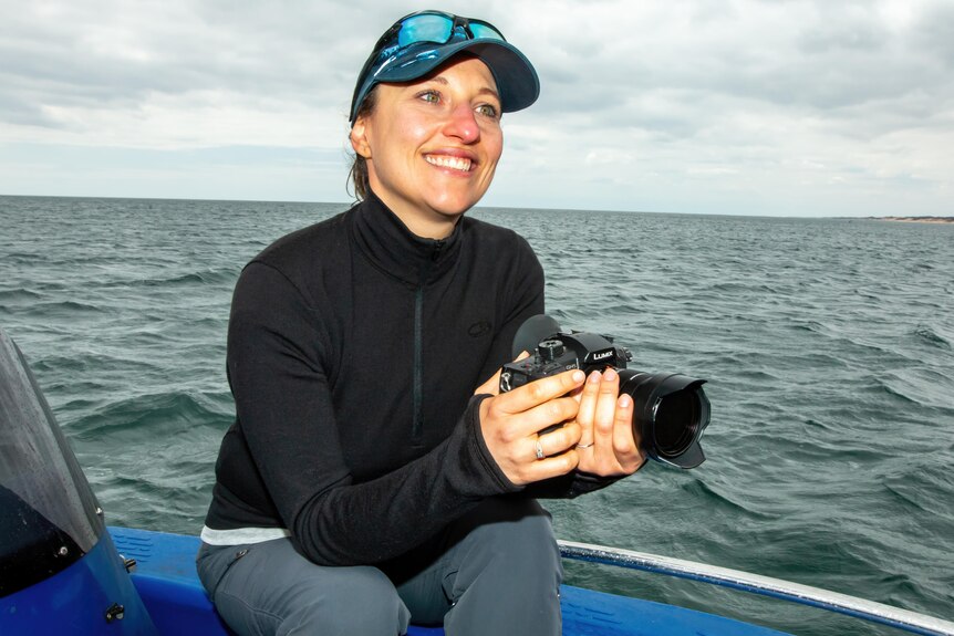 Dr Valeria Senigaglia sitting on a boat in the ocean on a grey cloudy day holding a camera and smiling 