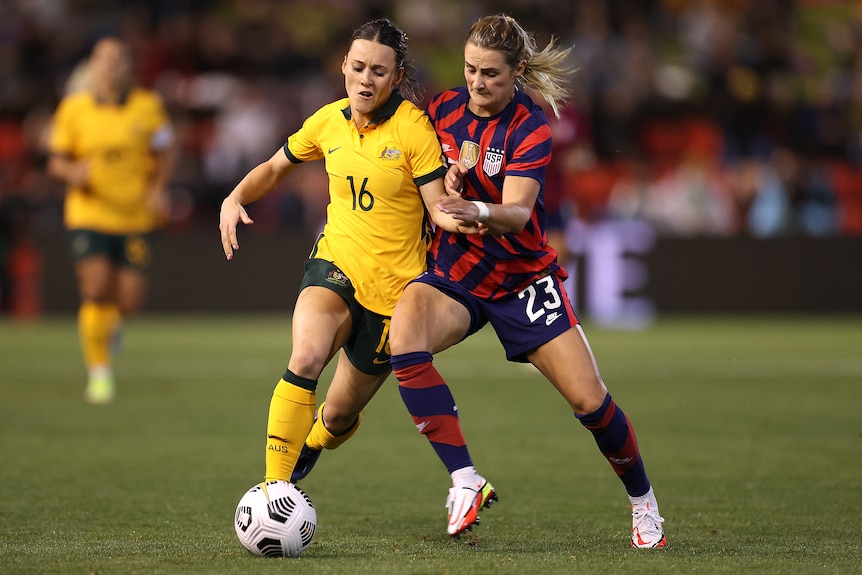A Matildas player attempts to dribble the ball while being challenged by a USA opponent.