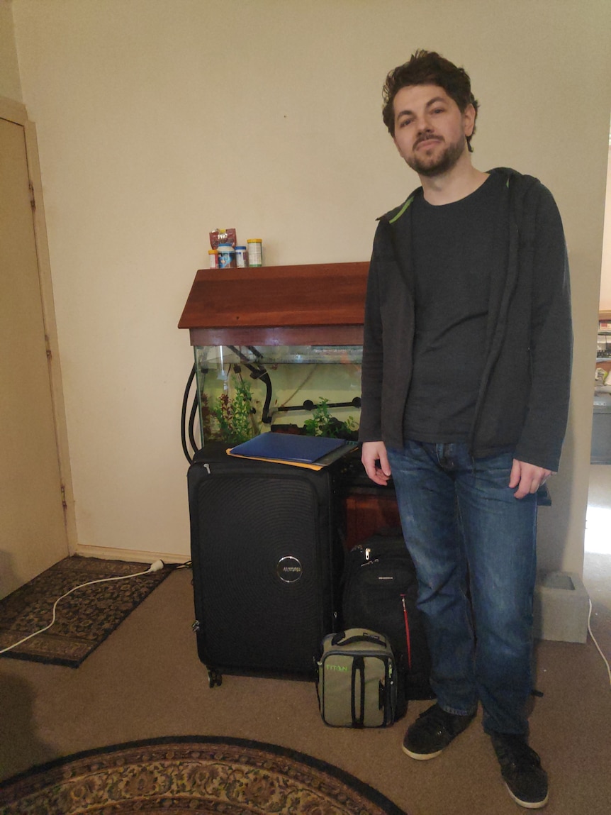 A young man stands in front of his packed bags.
