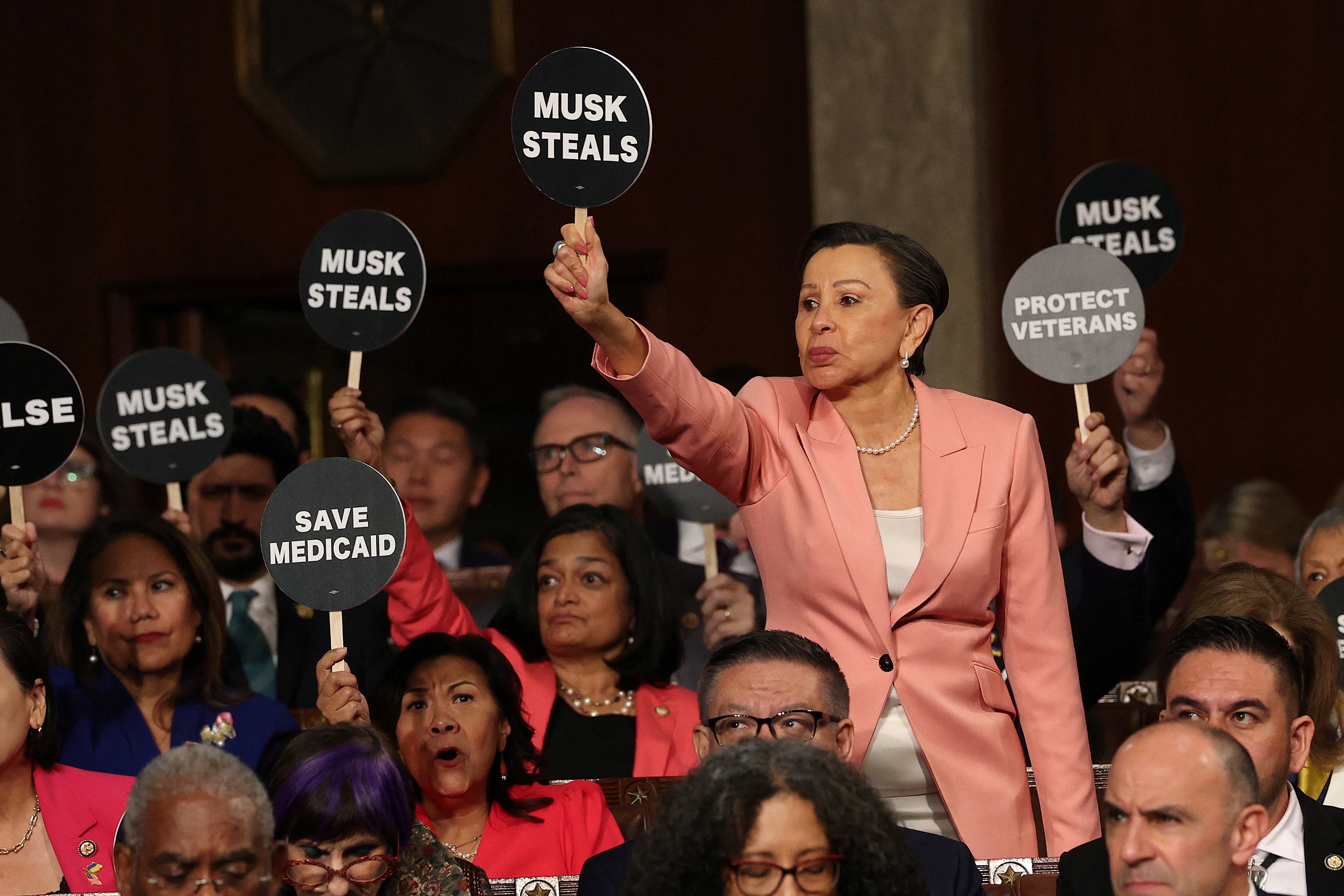 A woman holds a sign reading "MUSK STEALS" 