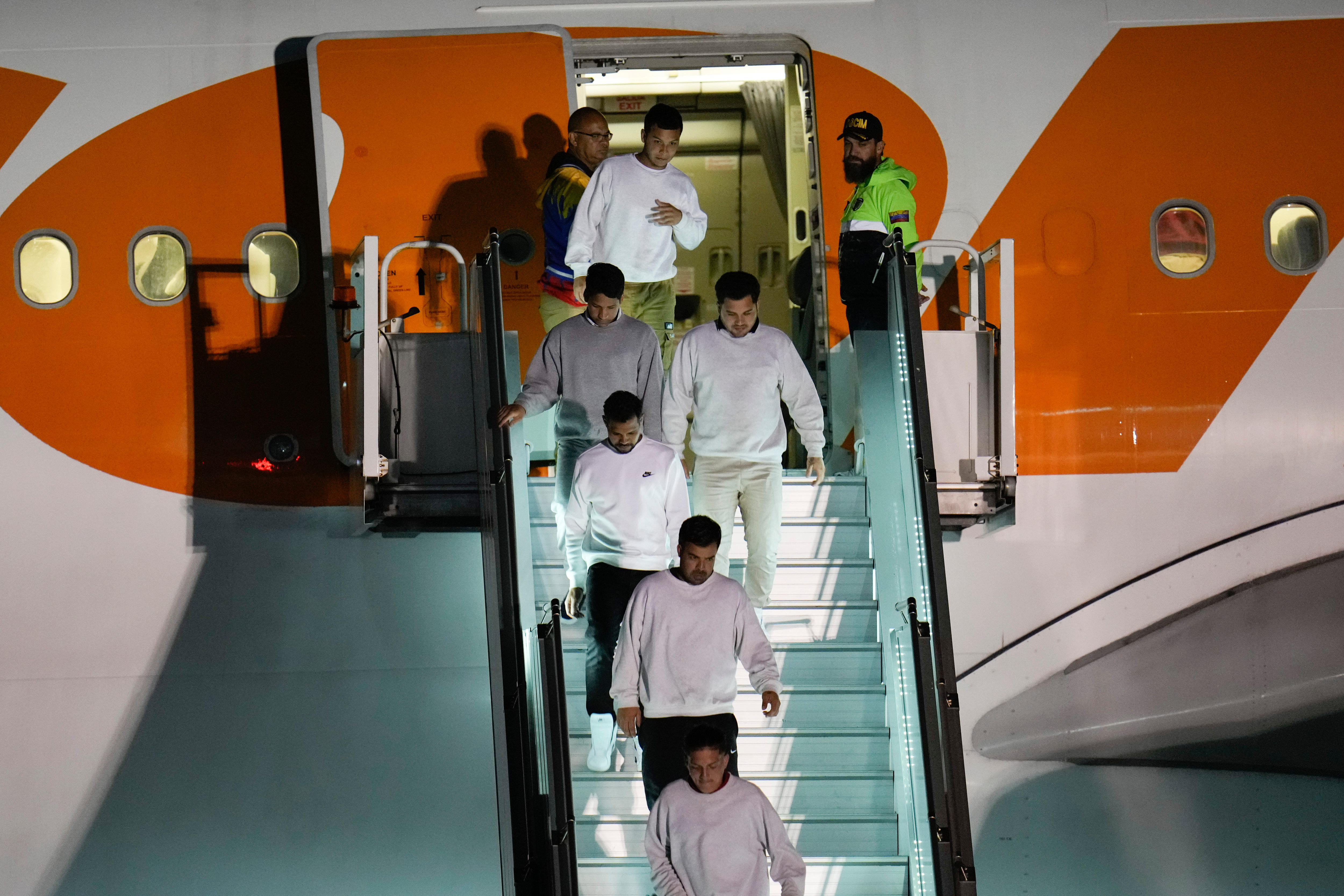 Men in white sweatsuits disembark a plane down boarding stairs 