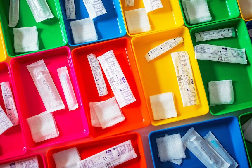 Coloured trays lined up with vaccine doses and clothes in them.