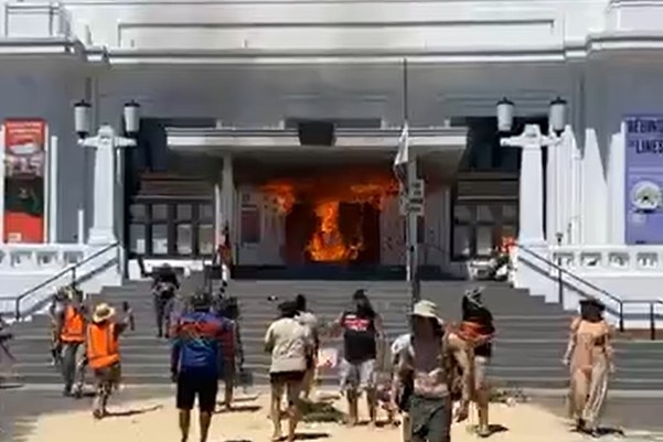 A crowd near a building's front door, which is burning.