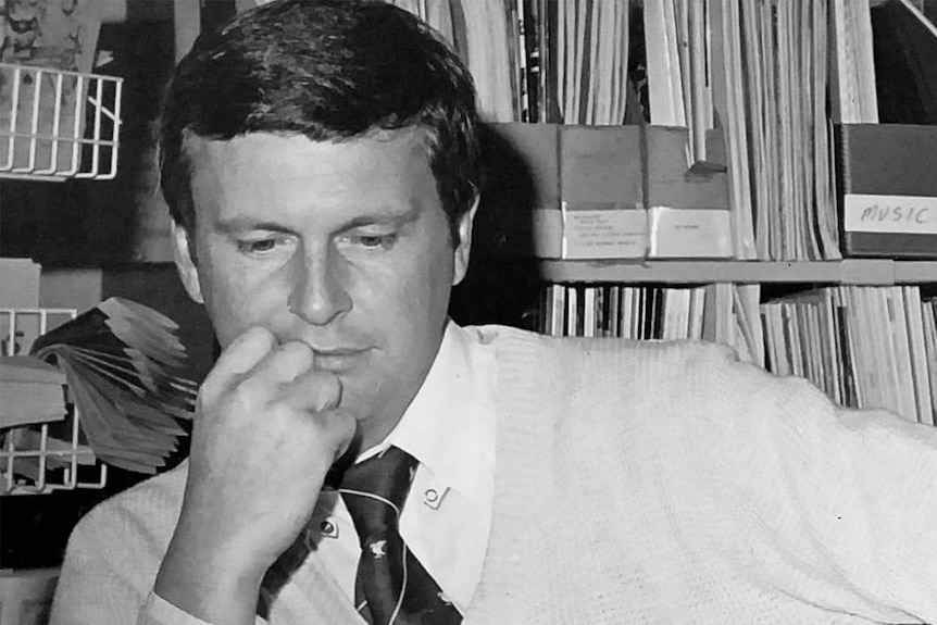 a black and white photograph of a man wearing a tie and sitting at a desk