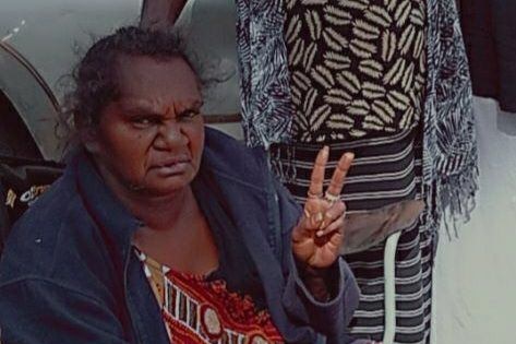 Indigenous woman sits on chair and displays peace sign with fingers