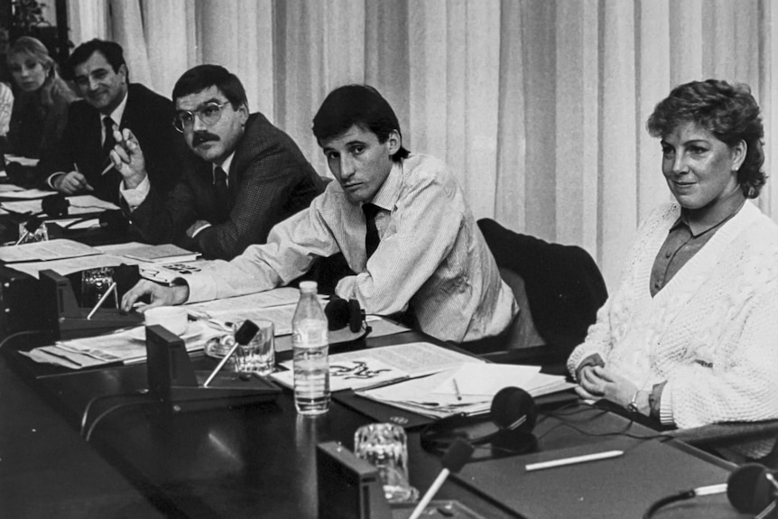 A group of Olympic athletes sit at a table at an IOC Congress meeting with pads of paper open on the desk in front of them.