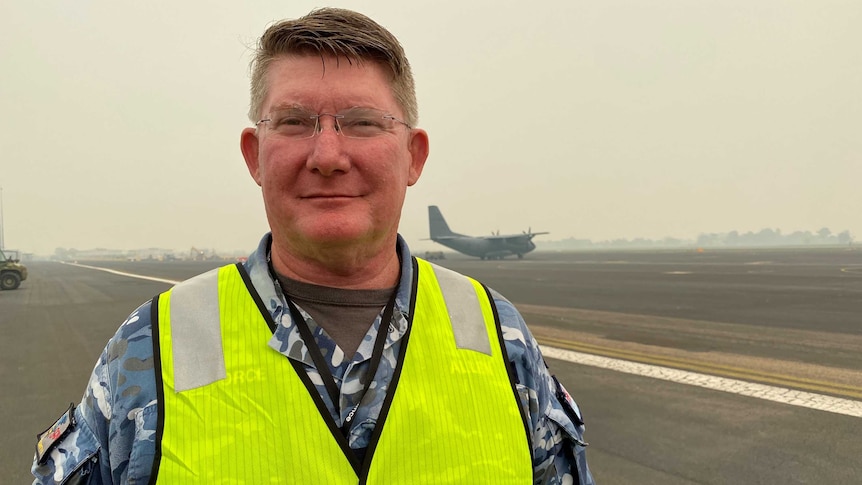 An air force commander stands on a runway in uniform