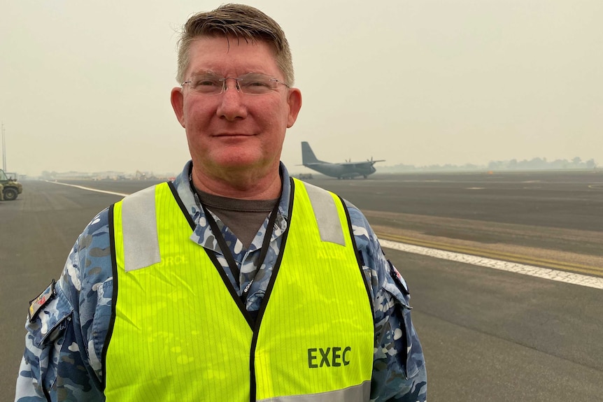 An air force commander stands on a runway in uniform