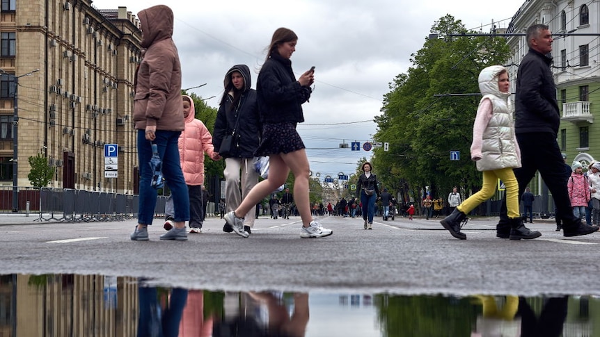 People cross the street in the centre of a Russian town, with reflections in a large puddle