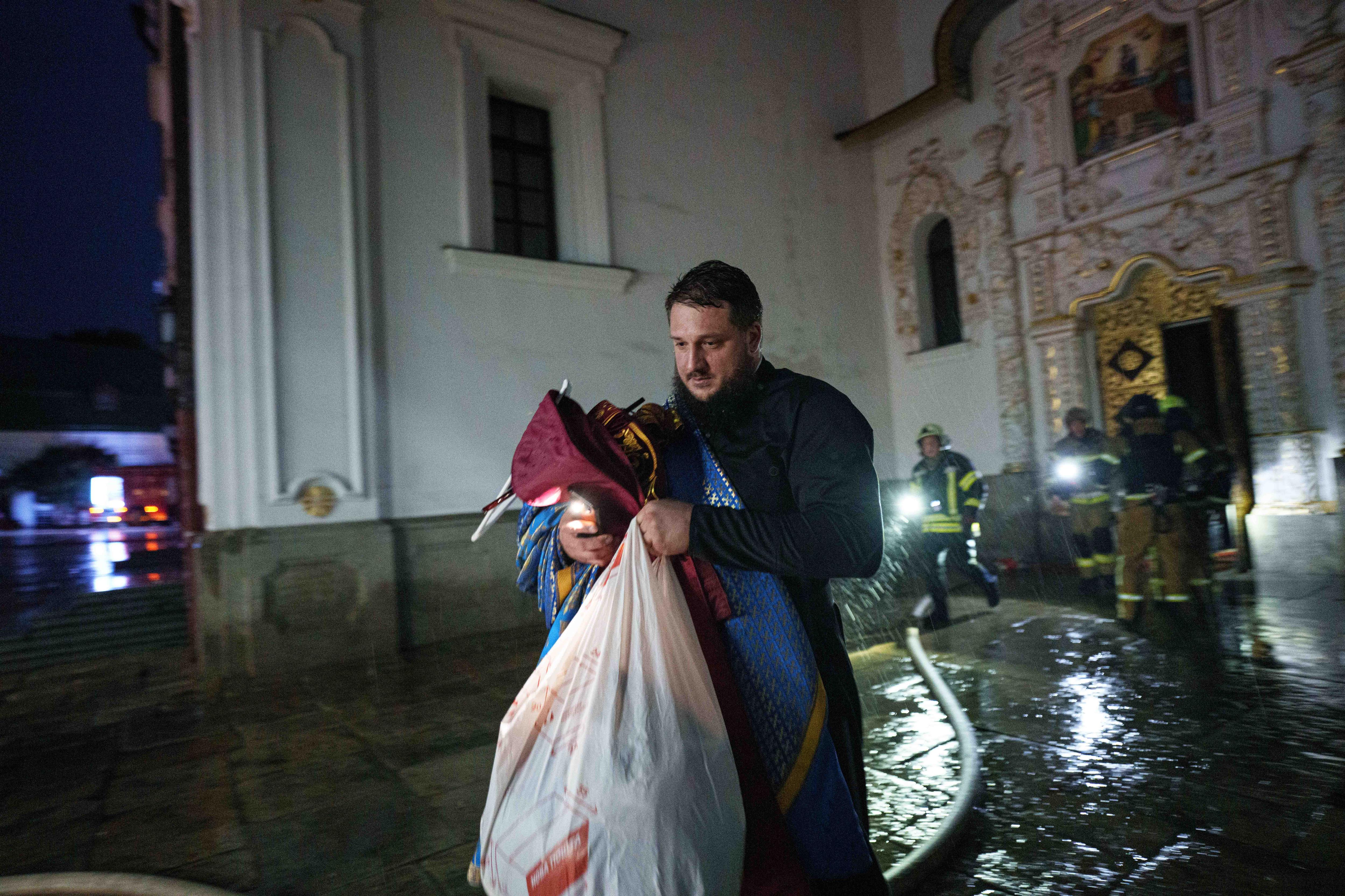 Priest carries a garbage bag of belongings out of a fire-damaged cathedral.