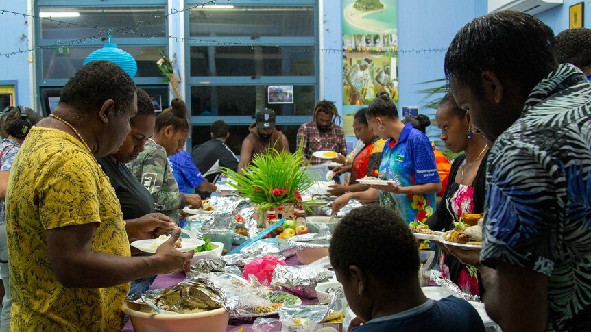 Men and women standing around a table filled with food.