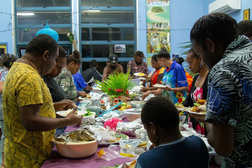 Men and women standing around a table filled with food.