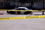 Police tape blocks a street where a police car can be seen in the background. 