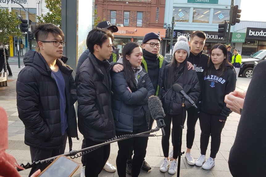 Eight friends of Thomas Tran standing in a group speaking to media with sad expressions on their faces.