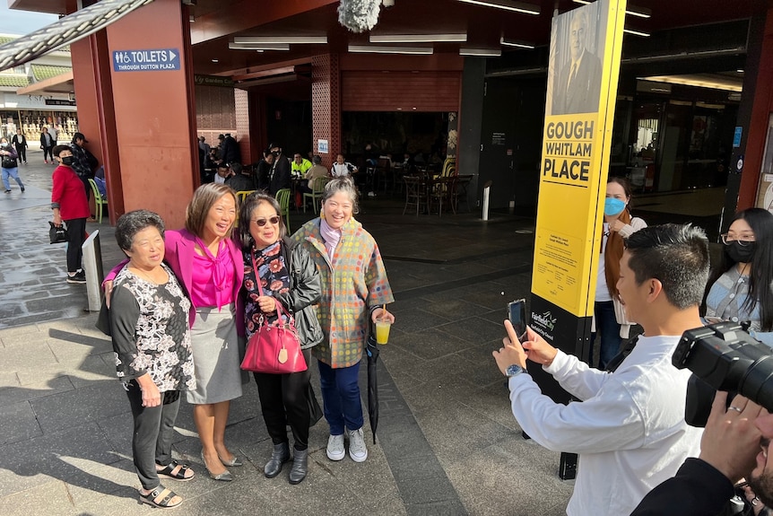 Four women smile for a man with a camera.