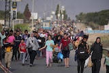 Hundreds of Palestinians walk on a road towards the camera, carrying backpacks and bags and children