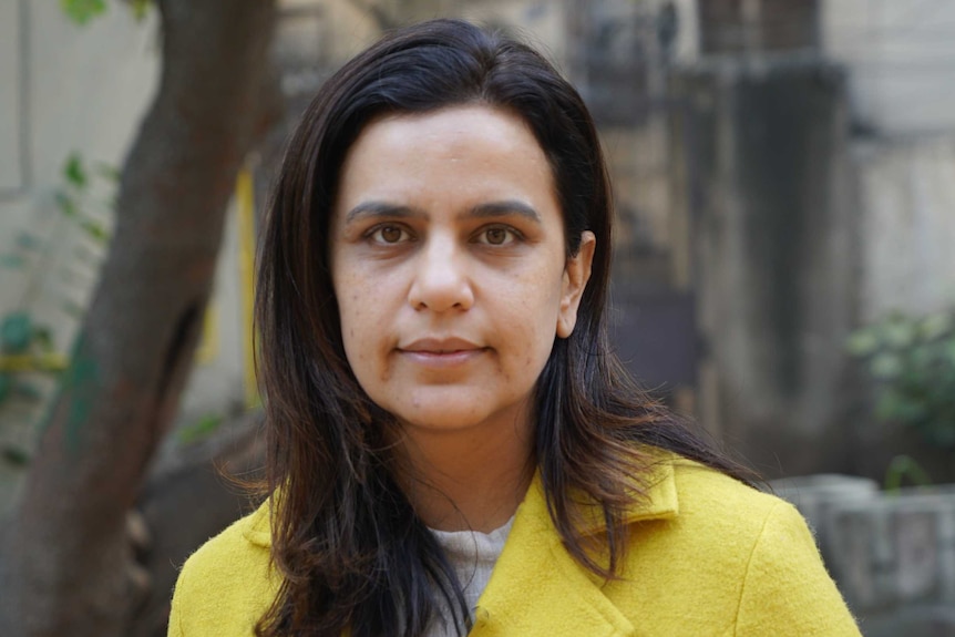 A woman in a yellow jacket looking seriously at the camera