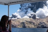 A woman on a boat takes a photo of a volcanic eruption.