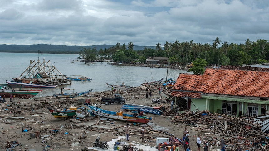 An Indonesian coastal village is pictured from above with streets flattened and debris strewn against a green building.