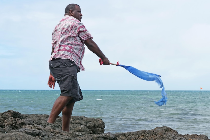  Man standing on rocks with water in background waving a blue flag.