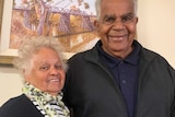 A woman and a man standing arm in arm in front of a painting