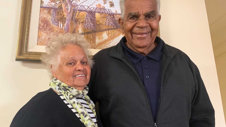 A woman and a man standing arm in arm in front of a painting