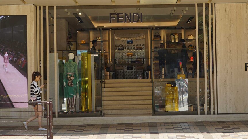 A young woman walks past a Fendi boutique, with no customers inside