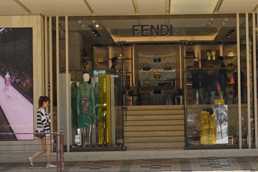 A young woman walks past a Fendi boutique, with no customers inside