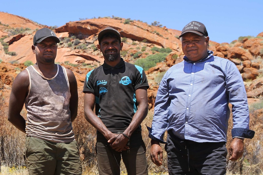 Four aboriginal Australians standing in front of a red rock in the outback