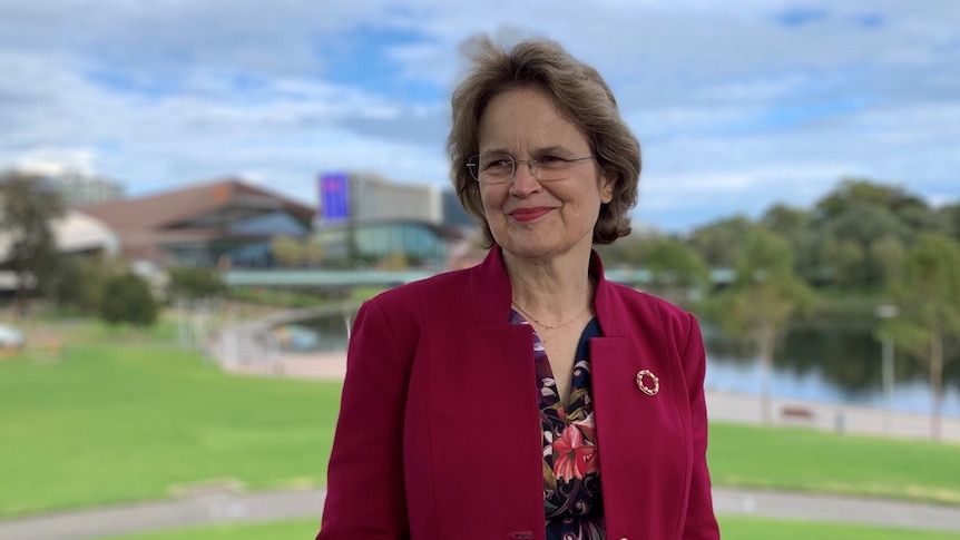 A woman wearing a red jacket in front of a park and river