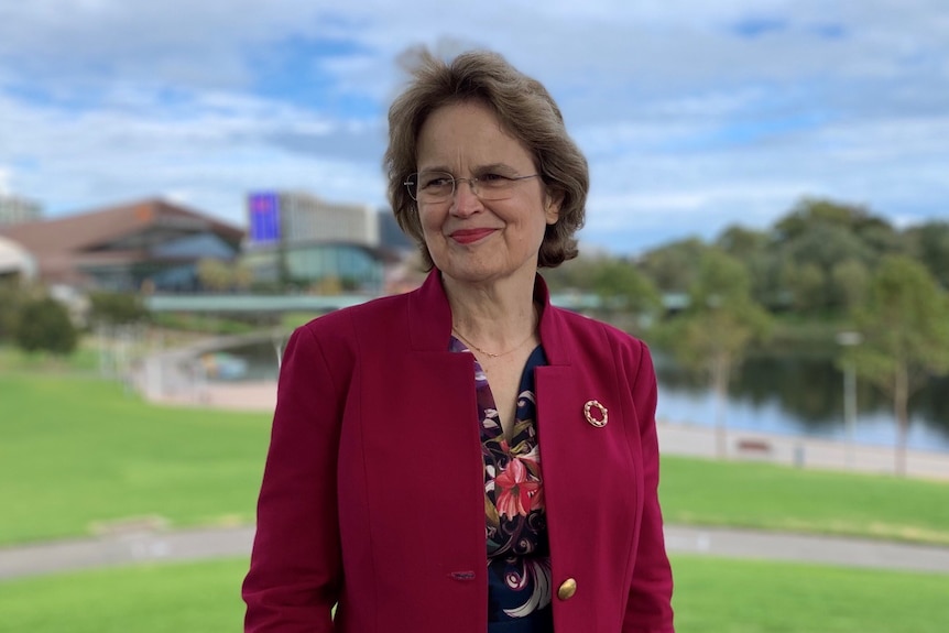 A woman wearing a red jacket in front of a park and river