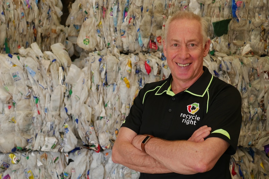 A man in a black polo shirt is pictured in front of recyclable material.