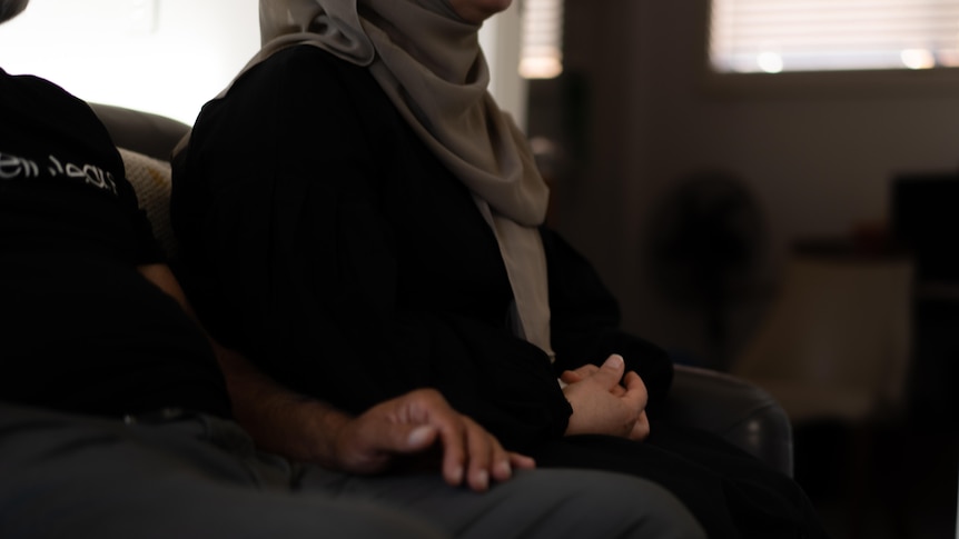 The hands of a man and woman are shown as they sit side by side on a couch.