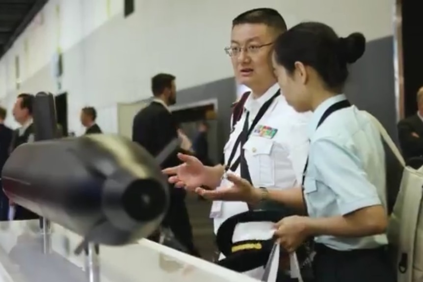 A man and a woman, both Chinese military personnel, inspect a model at  a navy conference.
