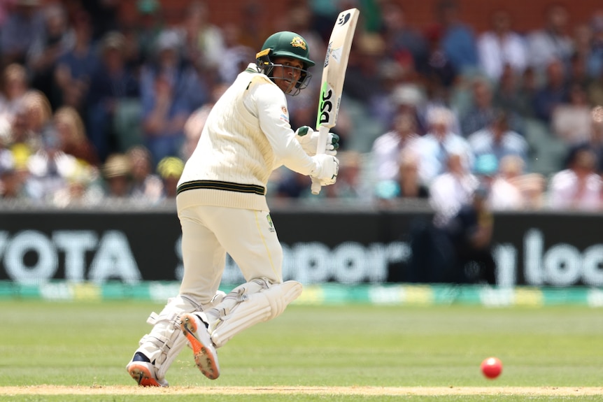 Usman Khawaja looks behind him at a cricket ball with his bat held up high