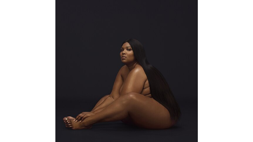 Lizzo sits naked against a dark background