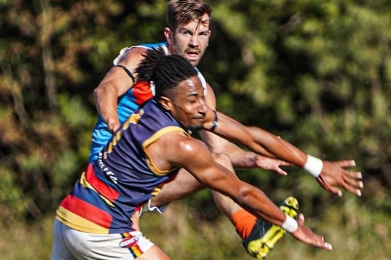 a man with his arms out in front of another man kicking the ball during an aussie rules match in Austin Texas.