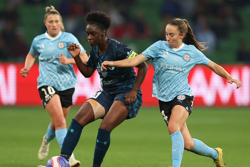 Footballer Princess Ibini controls the ball at her feet with two defenders converging on her